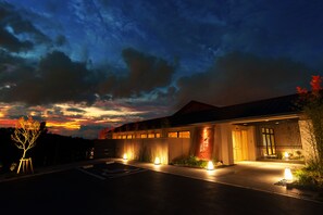 A modern building with a well-lit entrance, a parking area, and a landscaped garden. - Umino Ryotei Okinawa Nakamasou (Onna)