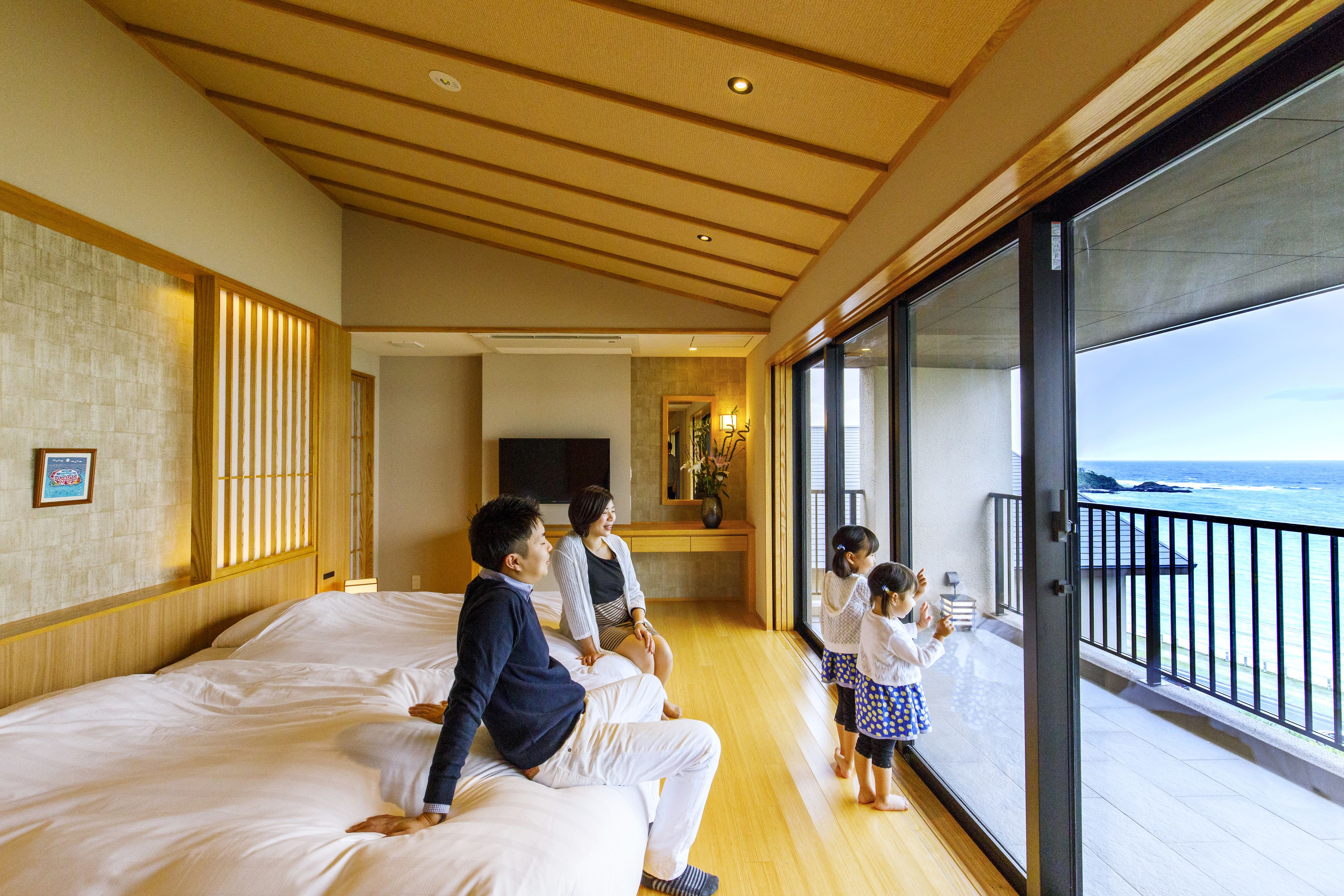 A hotel room with a large bed, a balcony with a view of the ocean, and a television in the corner.