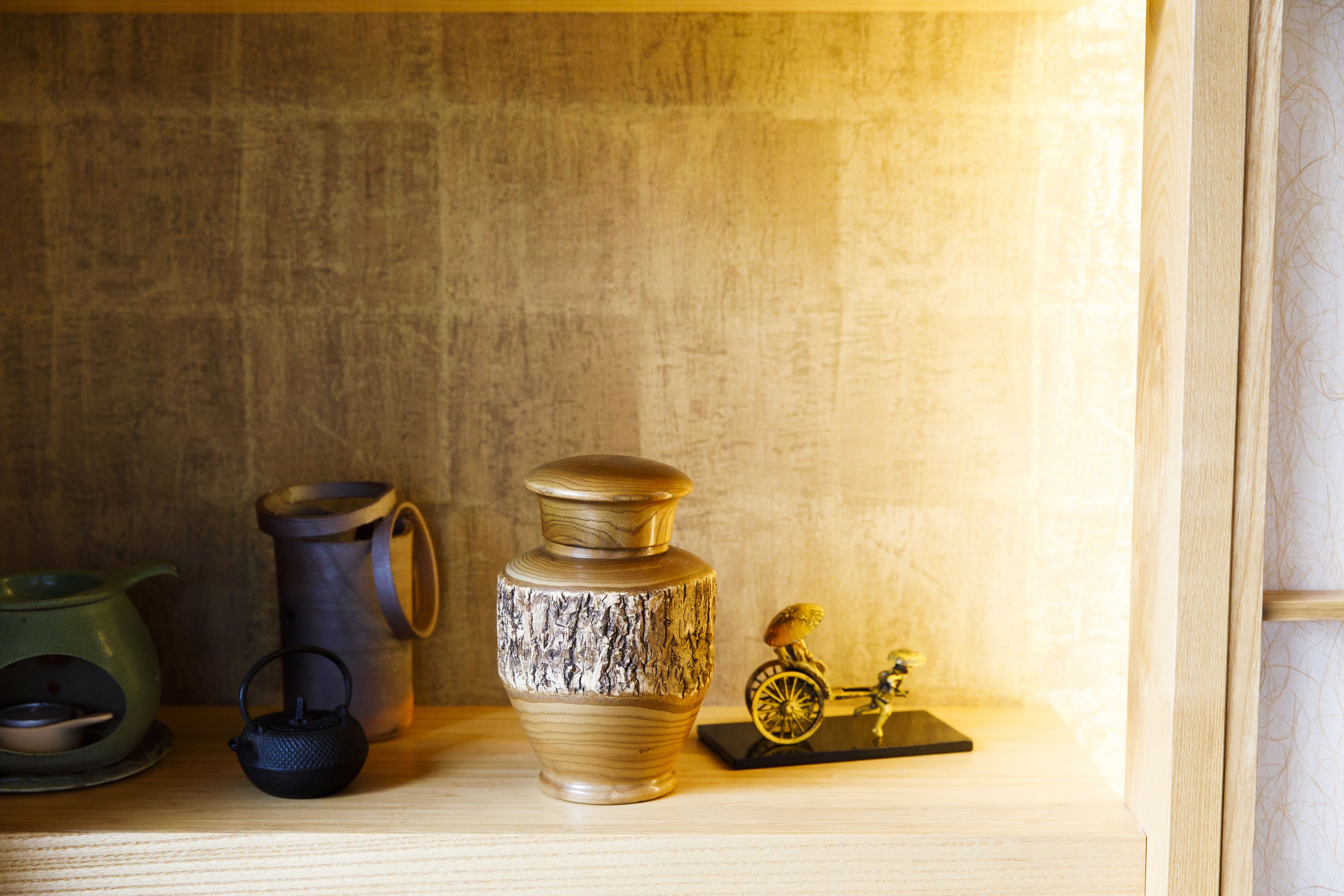 A shelf with a ceramic jug, a metal kettle, a green pot, and a small bicycle figurine.
