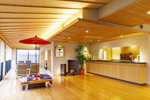 A spacious lobby with a reception desk, wooden flooring, a bench with blankets, and a large potted plant. - Umino Ryotei Okinawa Nakamasou (Onna)