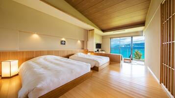 A modern hotel room with two beds, a wooden floor, a large window with a view, and a flat-screen TV.