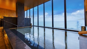 A modern indoor swimming pool with a view of the sky and clouds through large windows. - Umino Ryotei Okinawa Nakamasou (Onna)