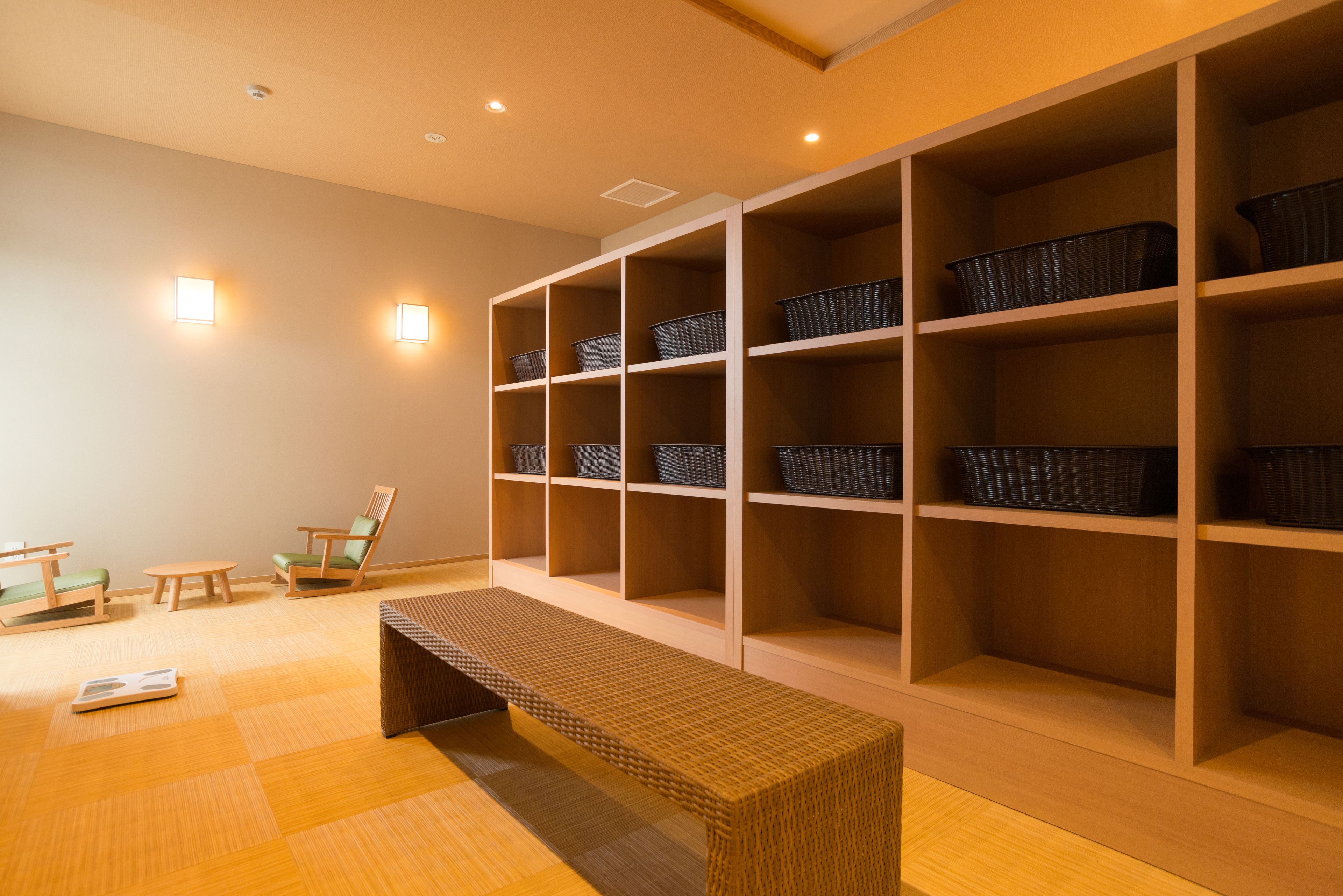 A room with a wooden bench, two chairs, and a wall with multiple shelves containing baskets.