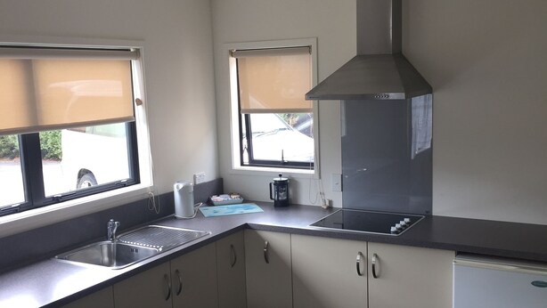 Una cocina moderna con lavavajillas integrado, un lavabo de acero inoxidable y una campana extractora. Se observan dos ventanas con persianas, y un ventilador de techo.