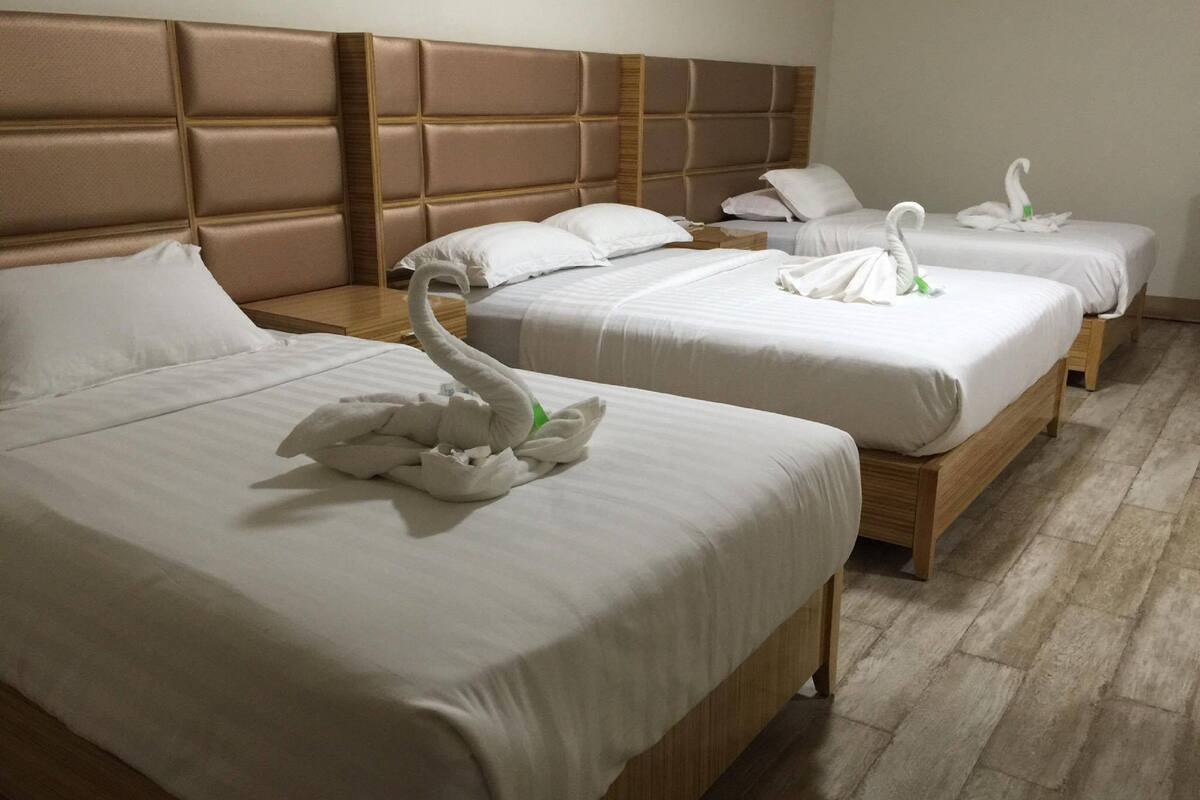 A hotel room with three beds, each with white bedding and a swan-shaped decoration.