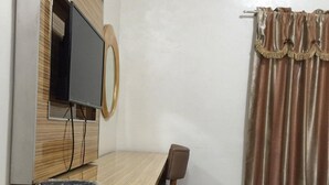 A room with a wooden desk, a television mounted on a wall, a chair, a bed, and a window with curtains. - Meaco Hotel - Solano (Solano)