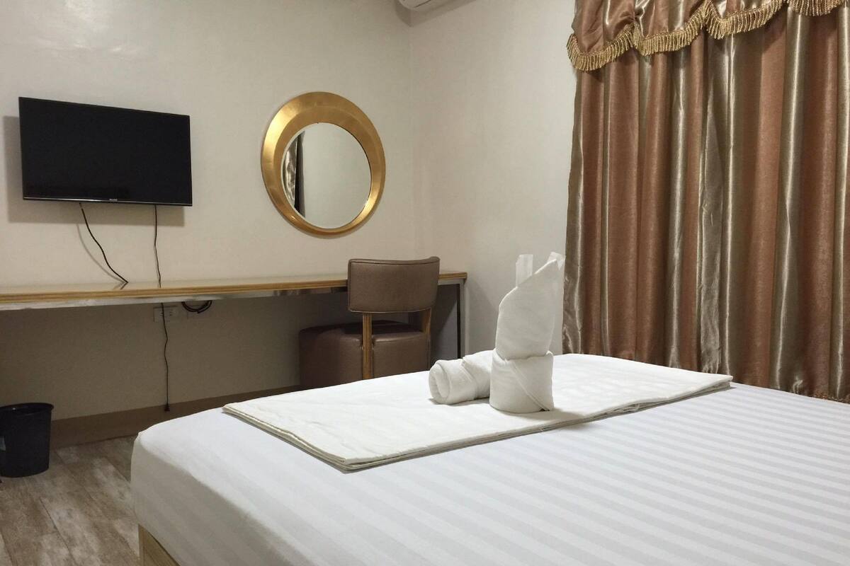 A hotel room with a bed, a desk, a chair, a television, and a mirror.