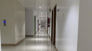 A long, well-lit corridor with white walls and a shiny floor, leading to multiple doors. - Meaco Hotel - Solano (Solano)