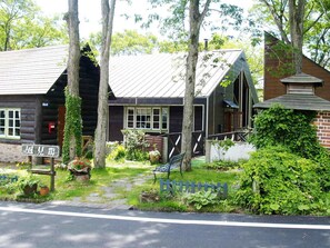 Un chalet rustique en rondins de bois, surmonté d’un toit en métal, entouré d’une végétation luxuriante et bordé d’un chemin pavé.