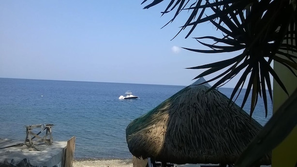 A beach view with a thatched umbrella and a boat on the water. - Meaco Hotel - Anilao (Mabini)