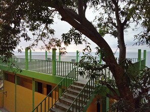 A staircase leading to a balcony overlooking a body of water, with a tree in the foreground. - Meaco Hotel - Anilao (Mabini)