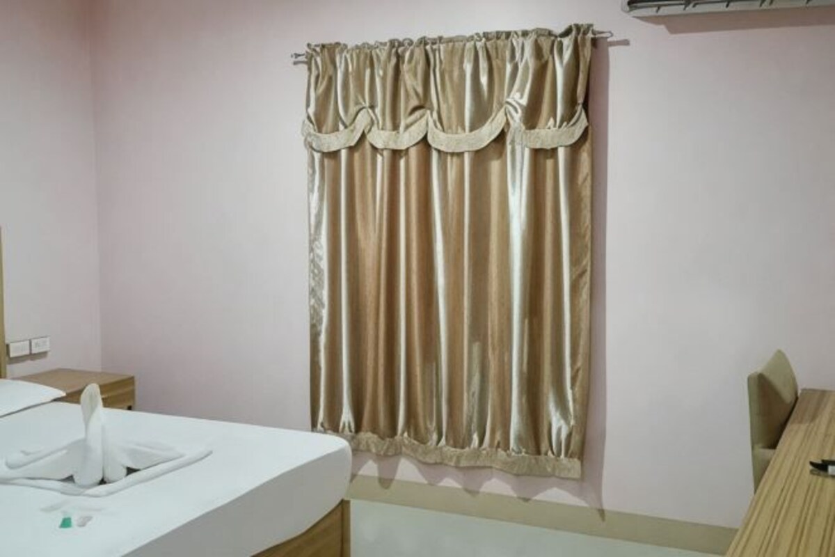 A hotel room with a bed, a bedside table, a chair, a desk, and a curtain.