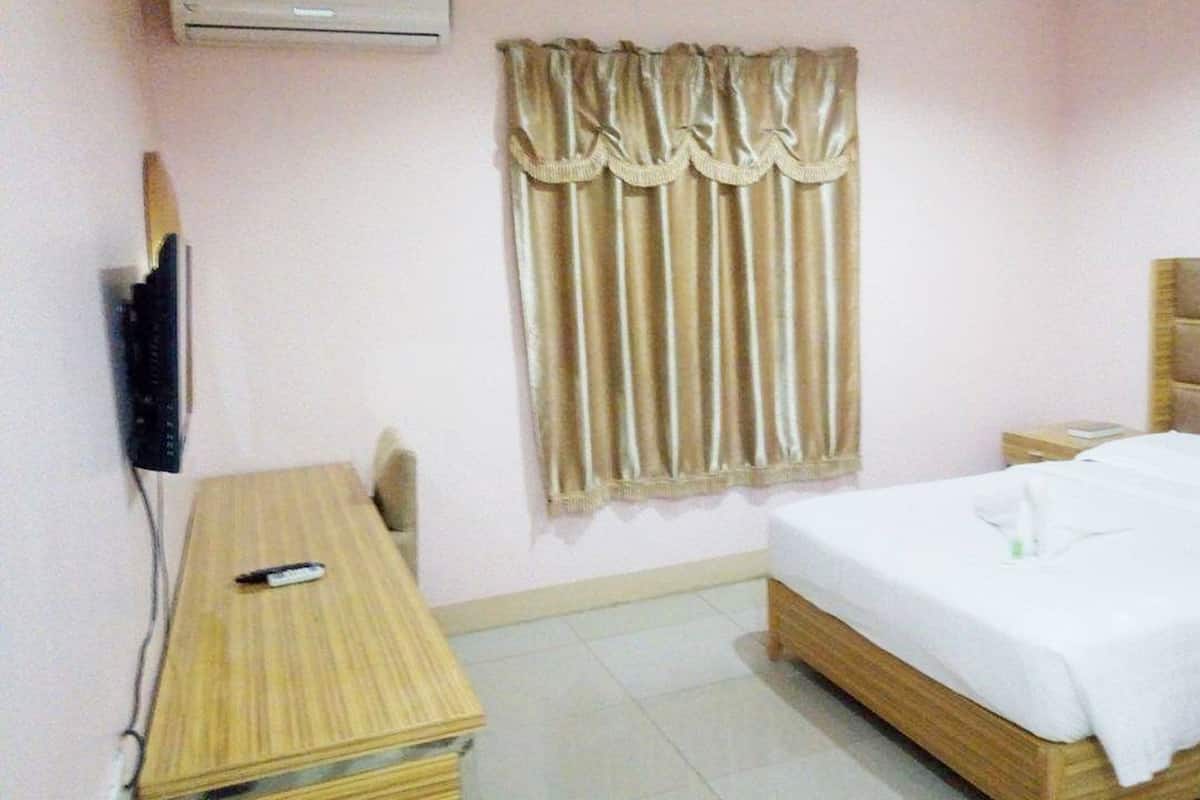A small hotel room with a single bed, a bedside table, a chair, a TV, and a window with curtains.