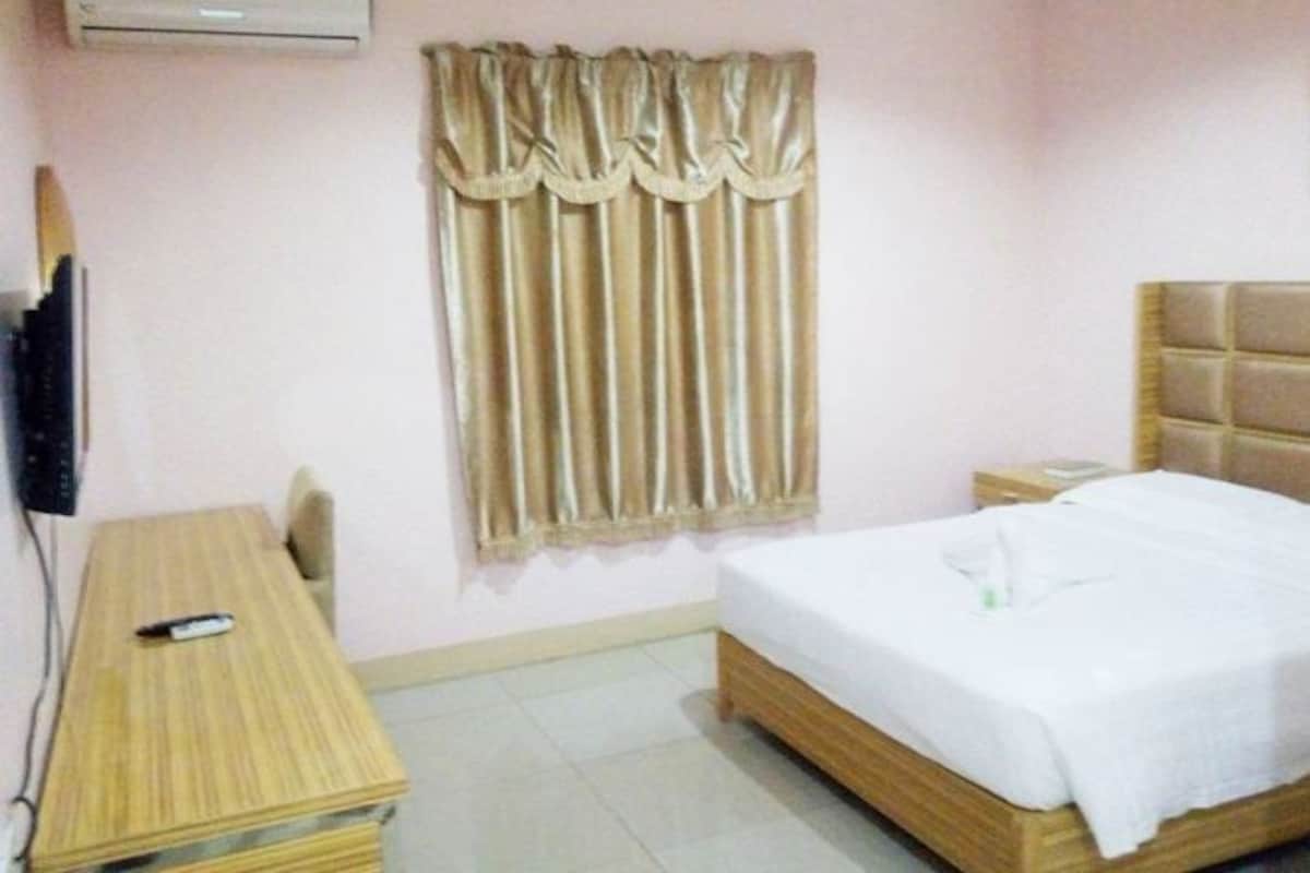 Habitación de hotel con una cama de madera, una mesita de noche, un televisor montado en la pared y una ventana con cortinas.