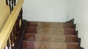 A staircase with alternating red and beige steps, wooden handrails, and a wall-mounted light fixture. - Meaco Hotel Legazpi (Legazpi)