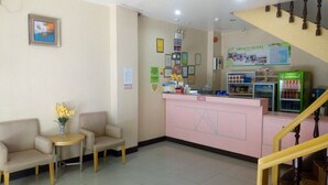 A reception area with a pink counter, a small table with chairs, a vase with flowers, and a staircase. - Meaco Hotel Legazpi (Legazpi)