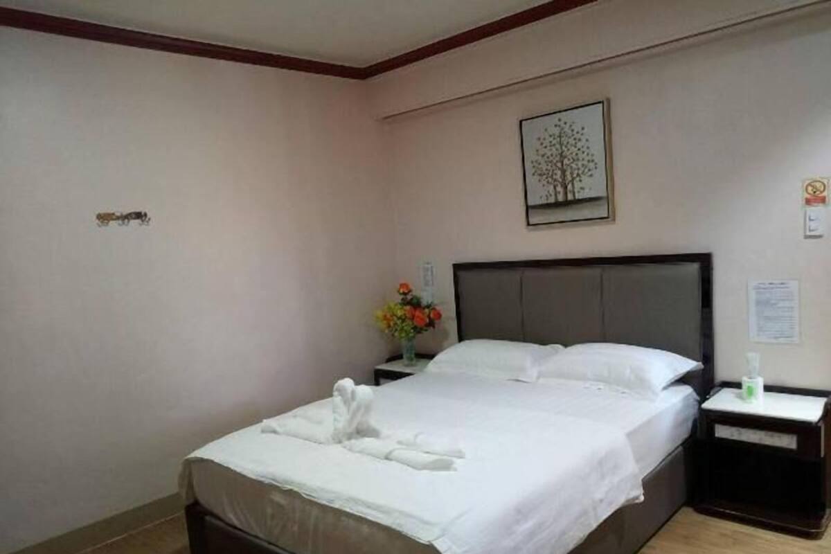 Una cama bien hecha con ropa blanca, una mesita de noche con un jarrón de flores y un cuadro en la pared.