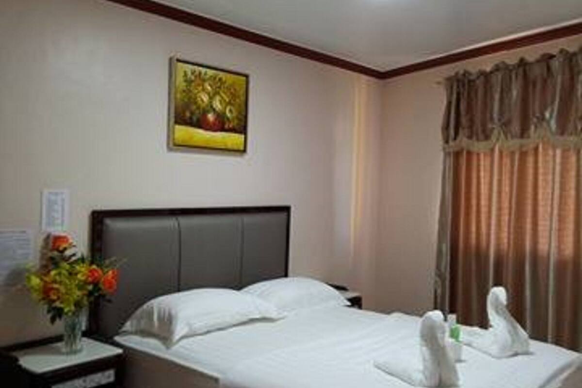 Una habitación de hotel con una cama, una mesita de noche, una silla, un cuadro en la pared y una ventana con cortinas.