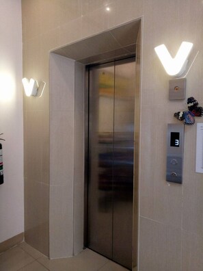 Een lift met een digitaal display waarop het cijfer 3 staat, een wandlamp en een vlinderdecoratie.