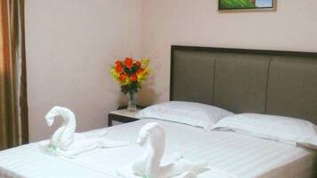 Ein Hotelzimmer mit einem ordentlich bezogenen Bett, einem Nachttisch mit Blumenvase und einem Gemälde an der Wand.
