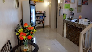 Una zona de recepción con un refrigerador lleno de bebidas, una barra con un menú y una pared decorada con certificados y avisos.