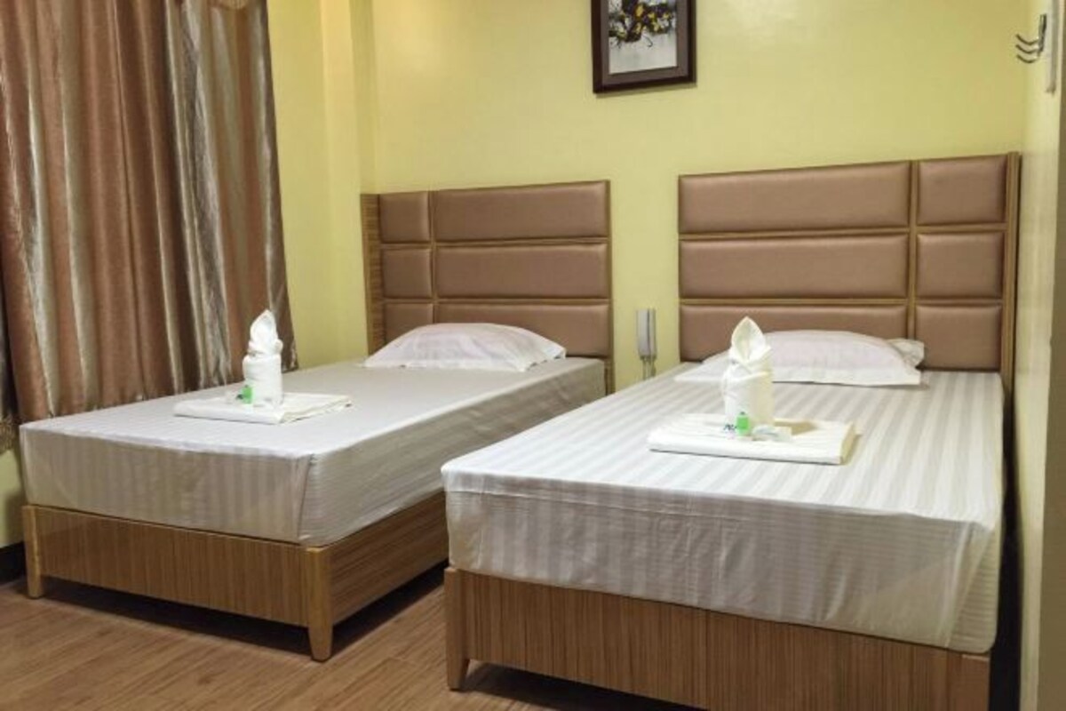Two single beds with headboards, a wooden floor, and a curtain on the left.