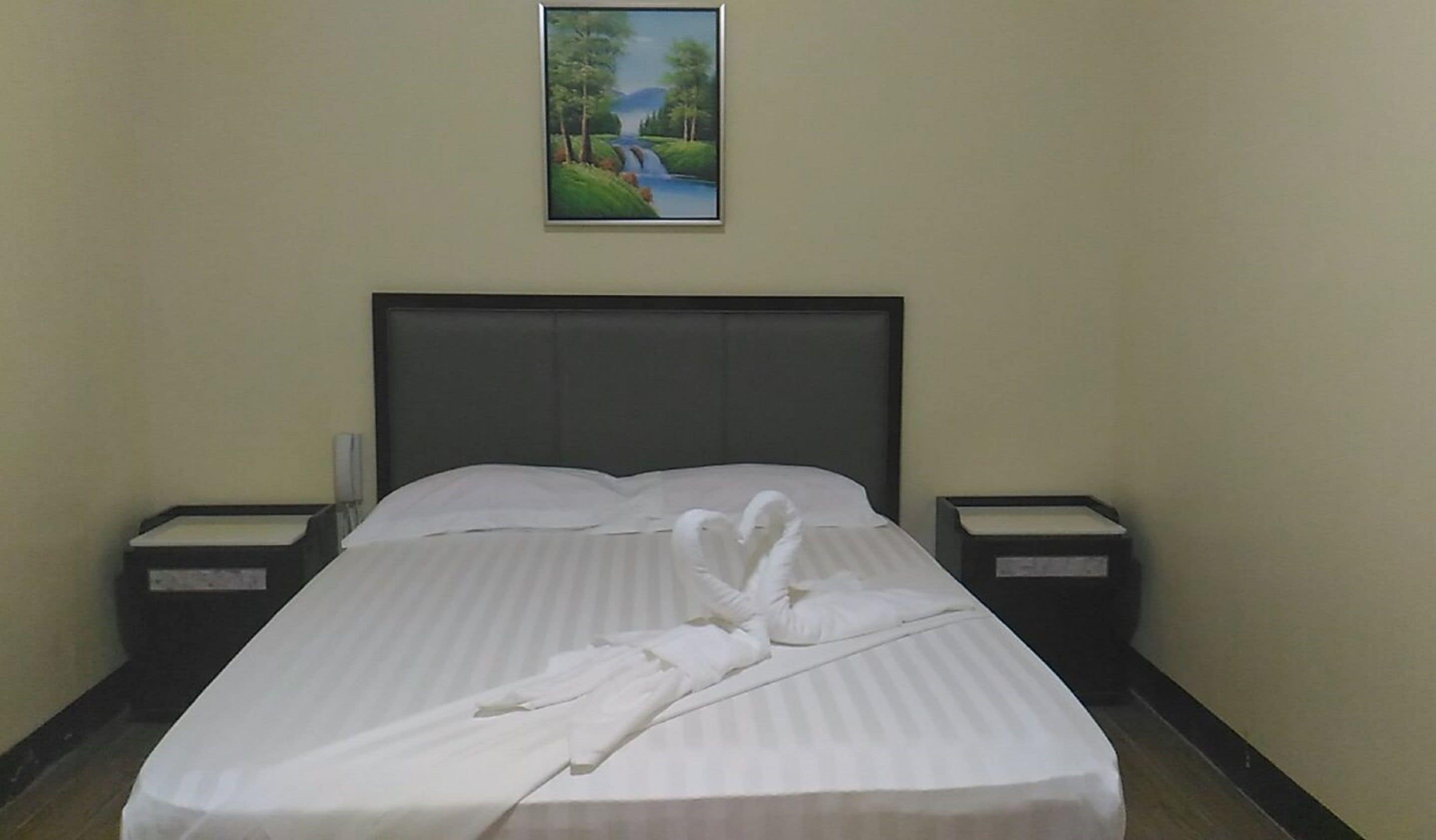 Habitación de hotel con una cama grande, dos mesitas de noche y un cuadro de un paisaje en la pared.