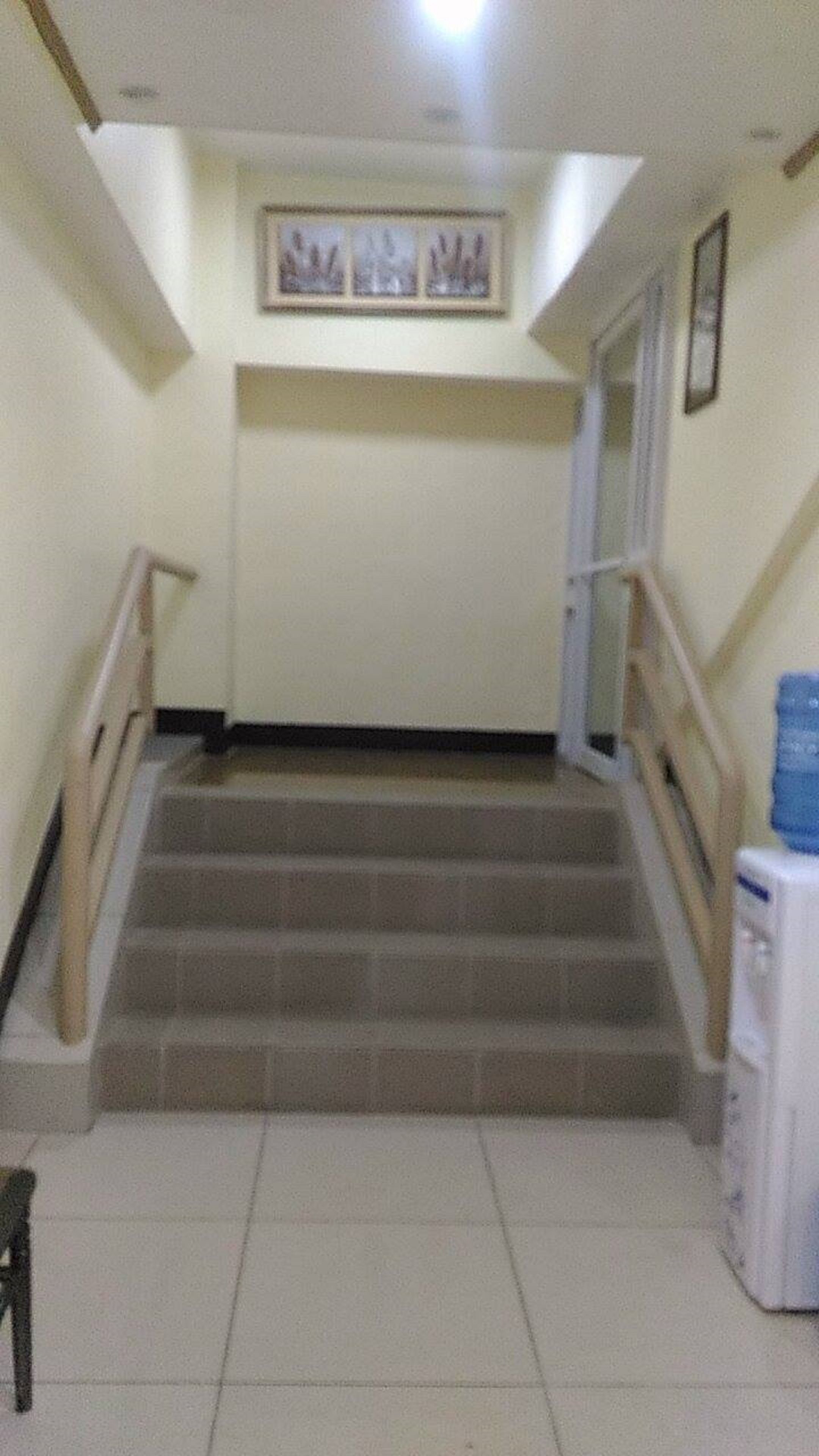 Una escala amb barana, un dispensador d'aigua i un quadre al mur.