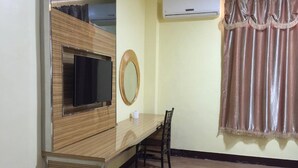 Une chambre d’hôtel équipée d’un bureau en bois, d’une télévision, d’un miroir, d’une chaise, d’un climatiseur et d’un rideau.