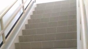 Un escalier carrelé de couleur beige, avec une main courante blanche.