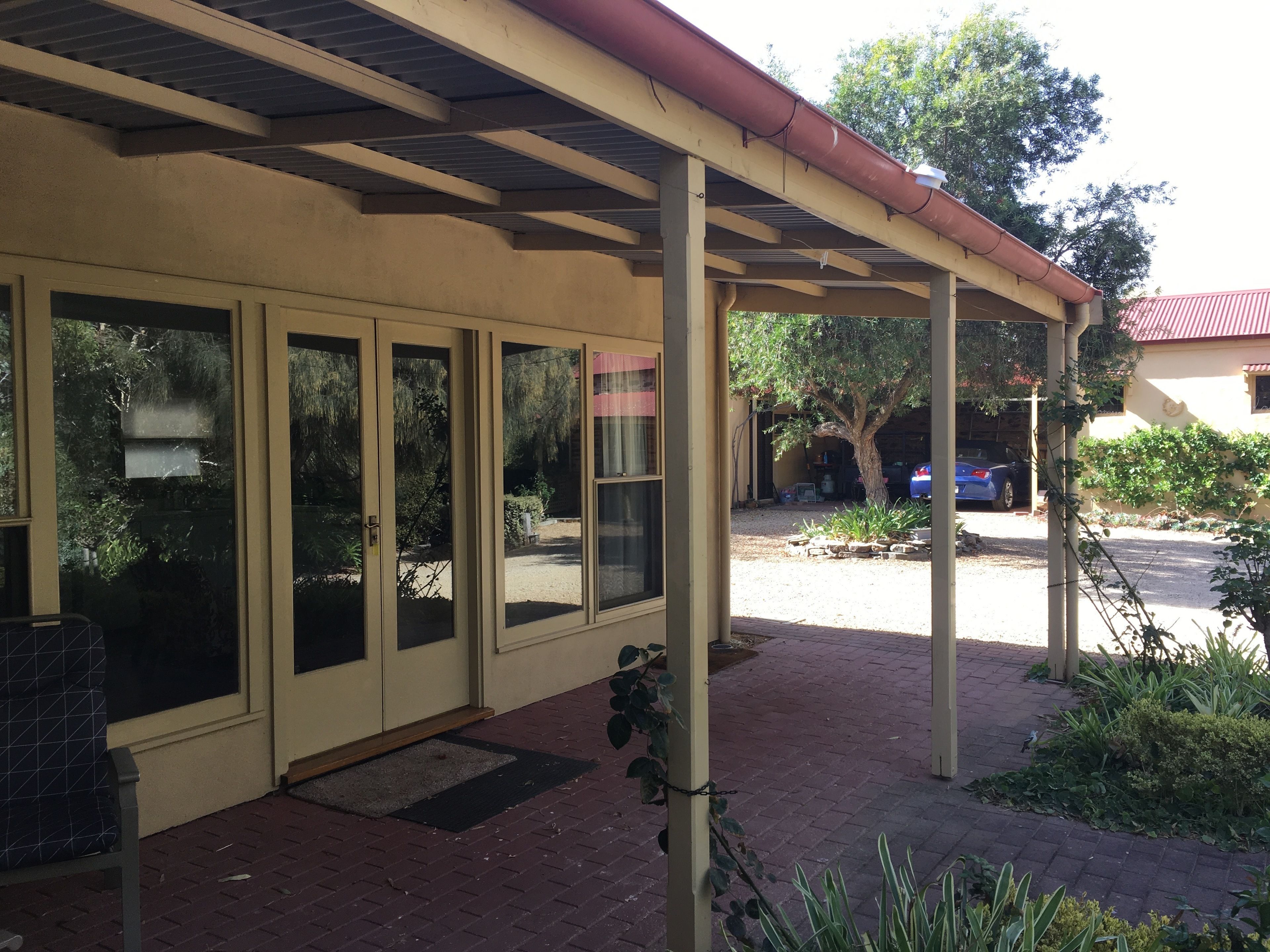 A covered outdoor area with a brick floor, large windows, and a red roof.
