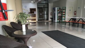 Un hall d'hôtel avec des meubles en osier, un comptoir d'accueil, une horloge, un extincteur et un distributeur automatique.