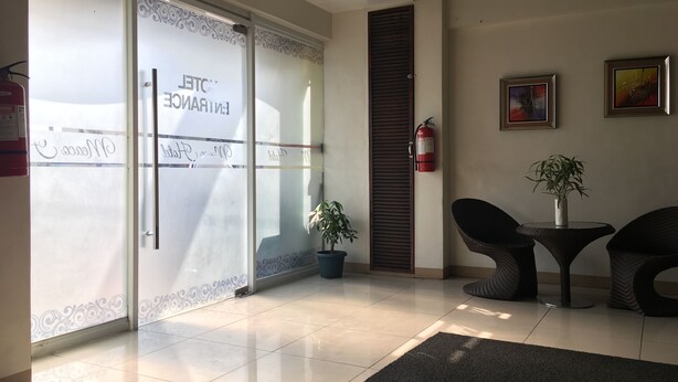 Un espace d’accueil avec une porte vitrée, un extincteur, une plante en pot et deux fauteuils en osier.