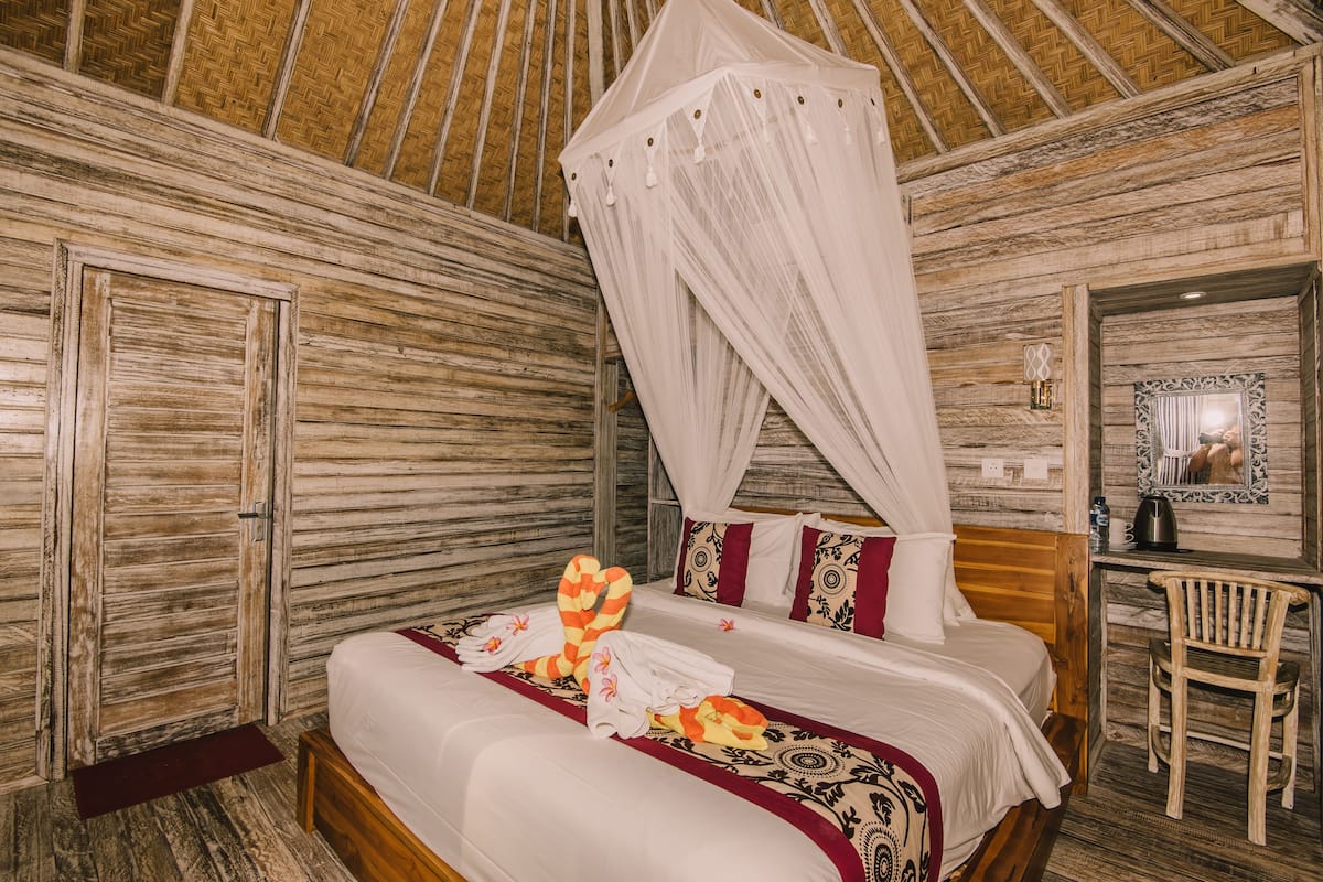 A wooden room with a bed, a chair, a mirror, and a mosquito net.