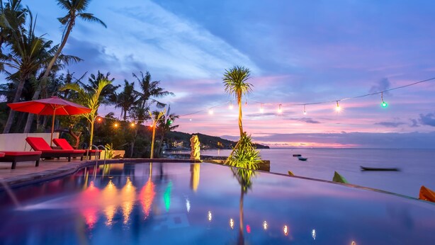 An infinity pool with a view of the ocean and palm trees at sunset. - The Bridge Huts (Ceningan Island)