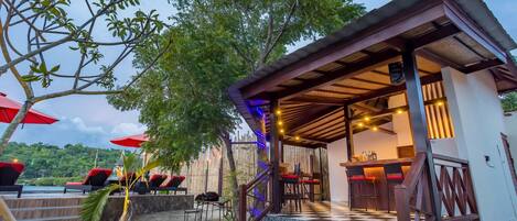 A covered outdoor seating area with a bar, stone steps, and red umbrellas.