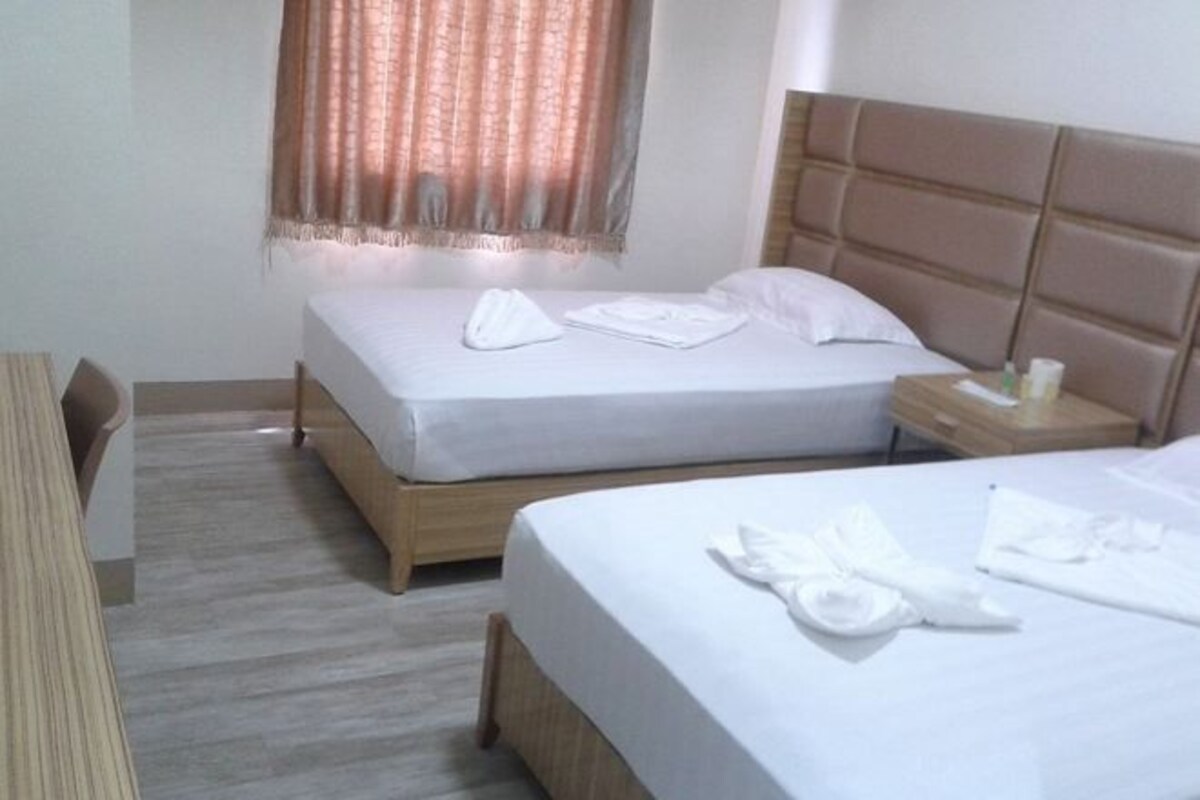Una habitación de hotel con dos camas, una mesita de noche de madera, un escritorio y una ventana con cortinas.