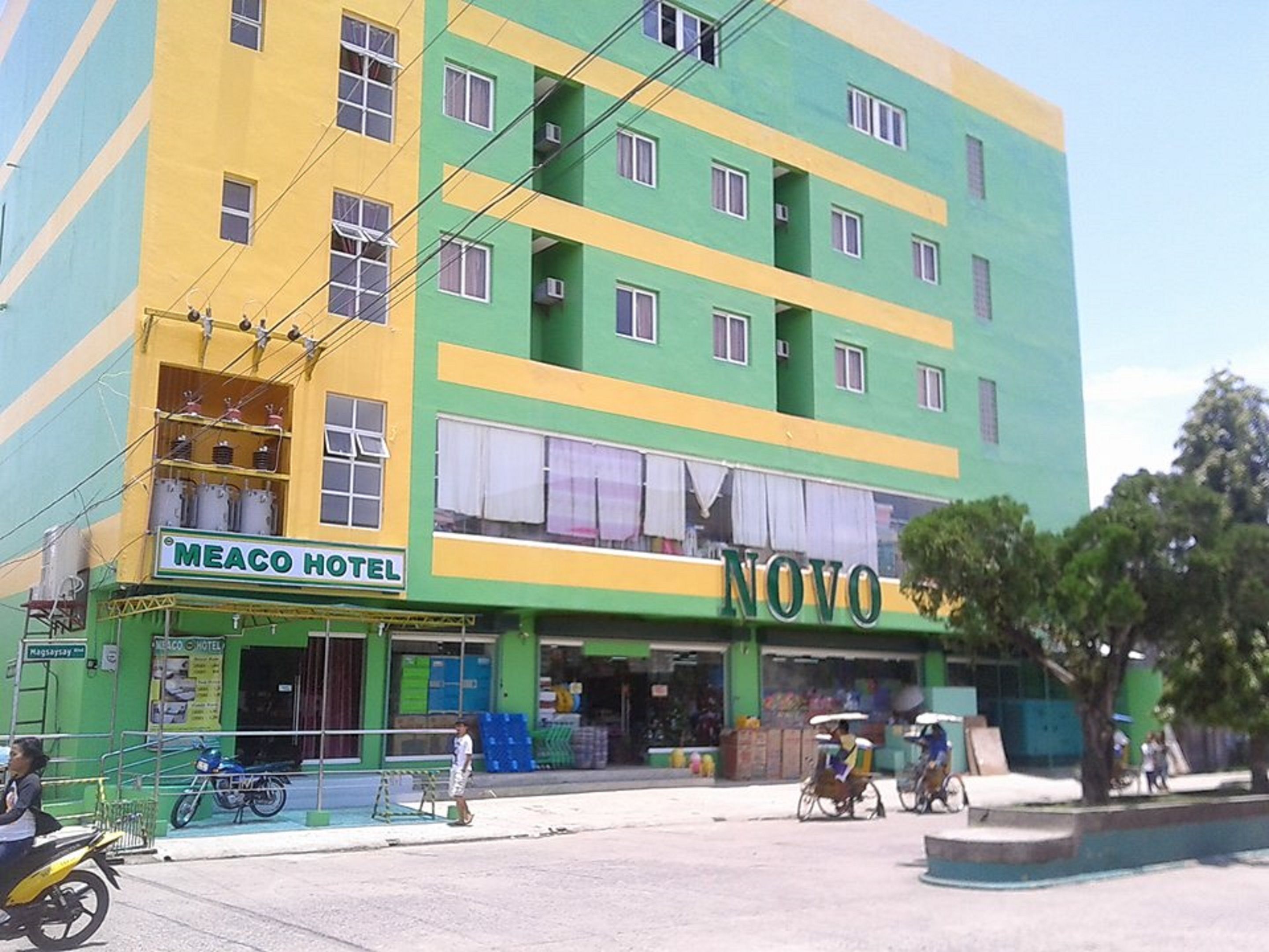 Un hotel de varios pisos con fachada verde y amarilla, llamado 'Meaco Hotel' y 'Novo'.