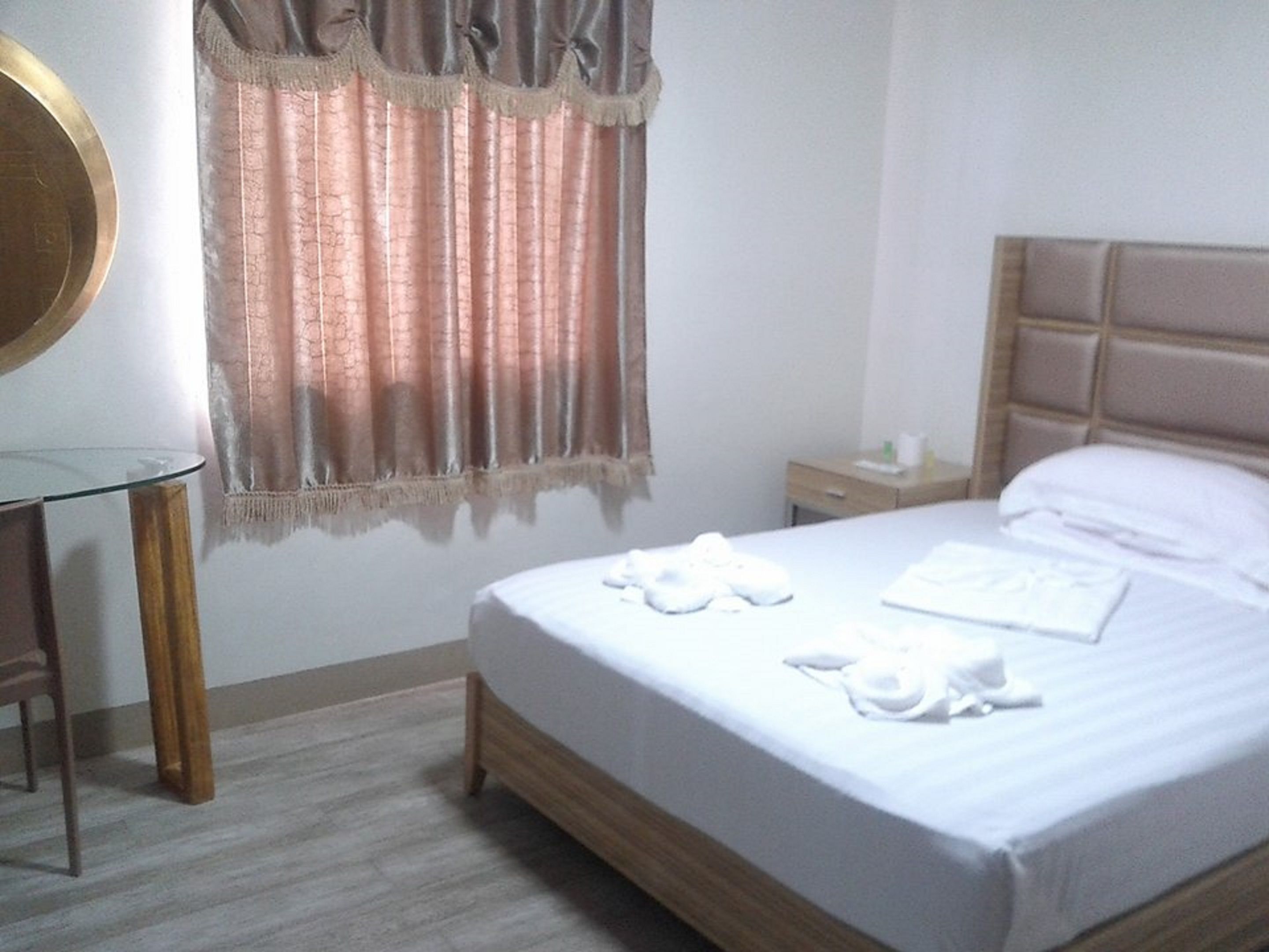Habitación de hotel con cama, mesita de noche, espejo y ventana con cortinas.