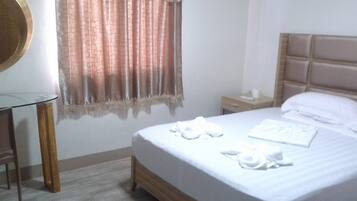 A hotel room with a bed, a bedside table, a nightstand, a mirror, and a window with curtains.