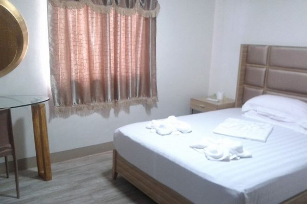 Una habitación de hotel con una cama, una mesita de noche, un espejo y una ventana con cortinas.