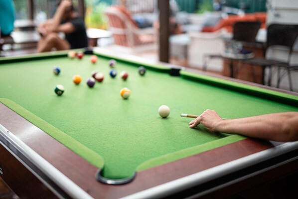 A pool table with balls and a cue stick, surrounded by chairs and tables in a casual setting. - Backpackers Newcastle (Hamilton East)