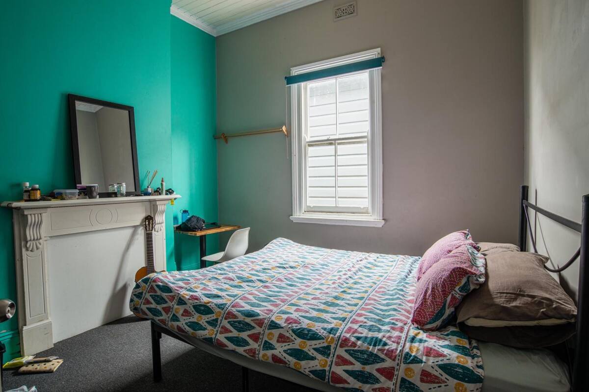 Un dormitorio con cama, ventana, espejo, escritorio y silla.