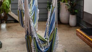 A hammock suspended from a wooden beam in a covered outdoor area with potted plants around. - Backpackers Newcastle (Hamilton East)