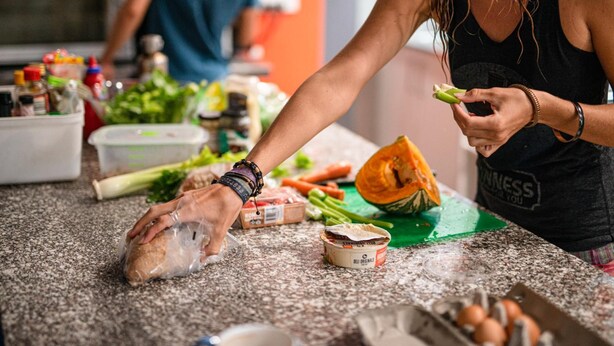 A person preparing food on a kitchen counter with various vegetables and packaged items. - Backpackers Newcastle (Hamilton East)