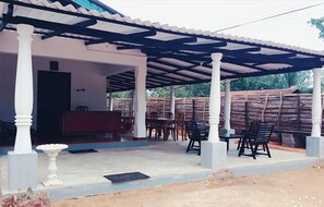 A covered outdoor seating area with tables and chairs, a white column, and a red counter. - Ladun Sigiri Villa (Sigiriya)