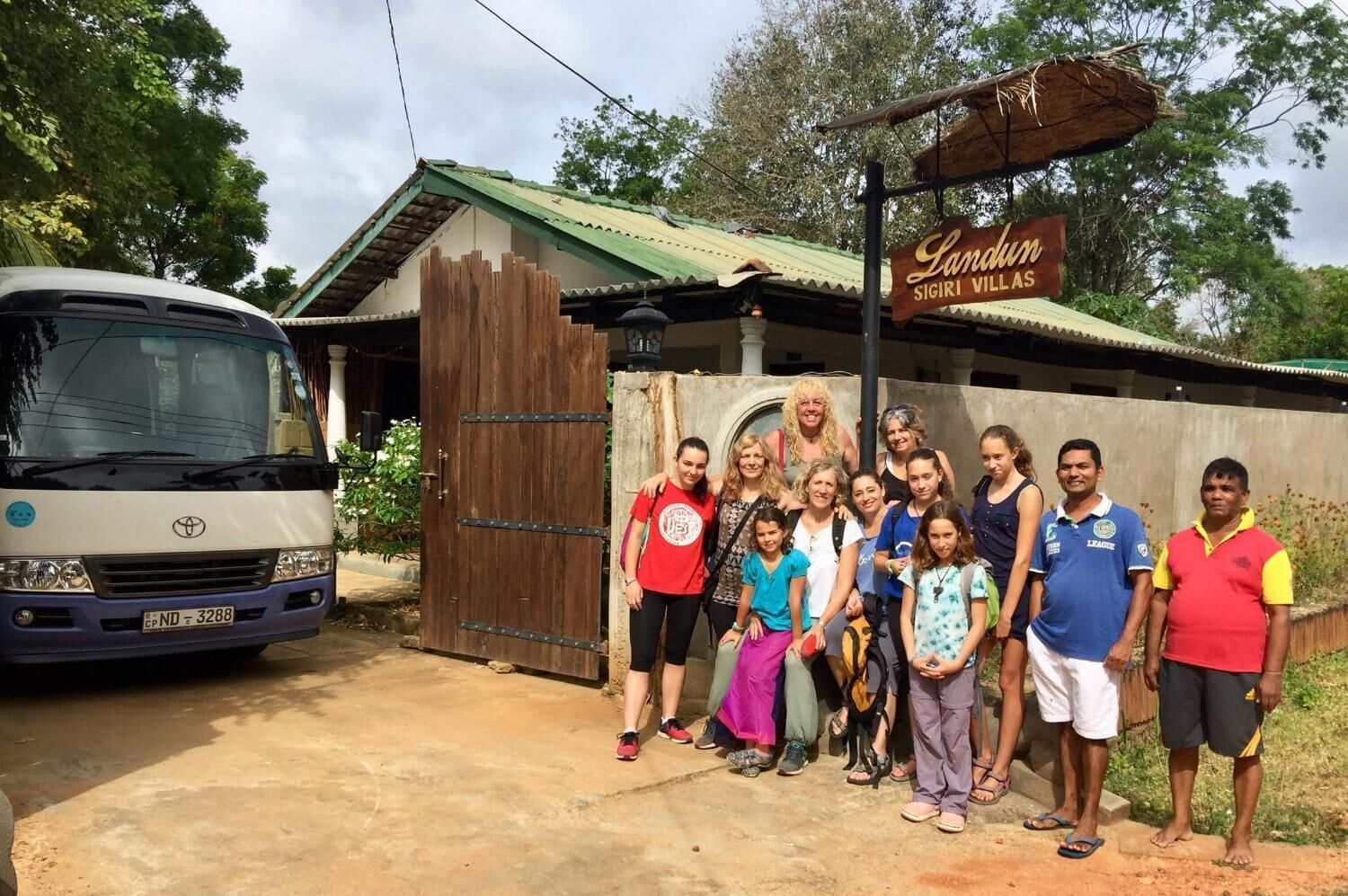 A group of people standing in front of a building with a sign that reads "Landrum Sigiri Village."