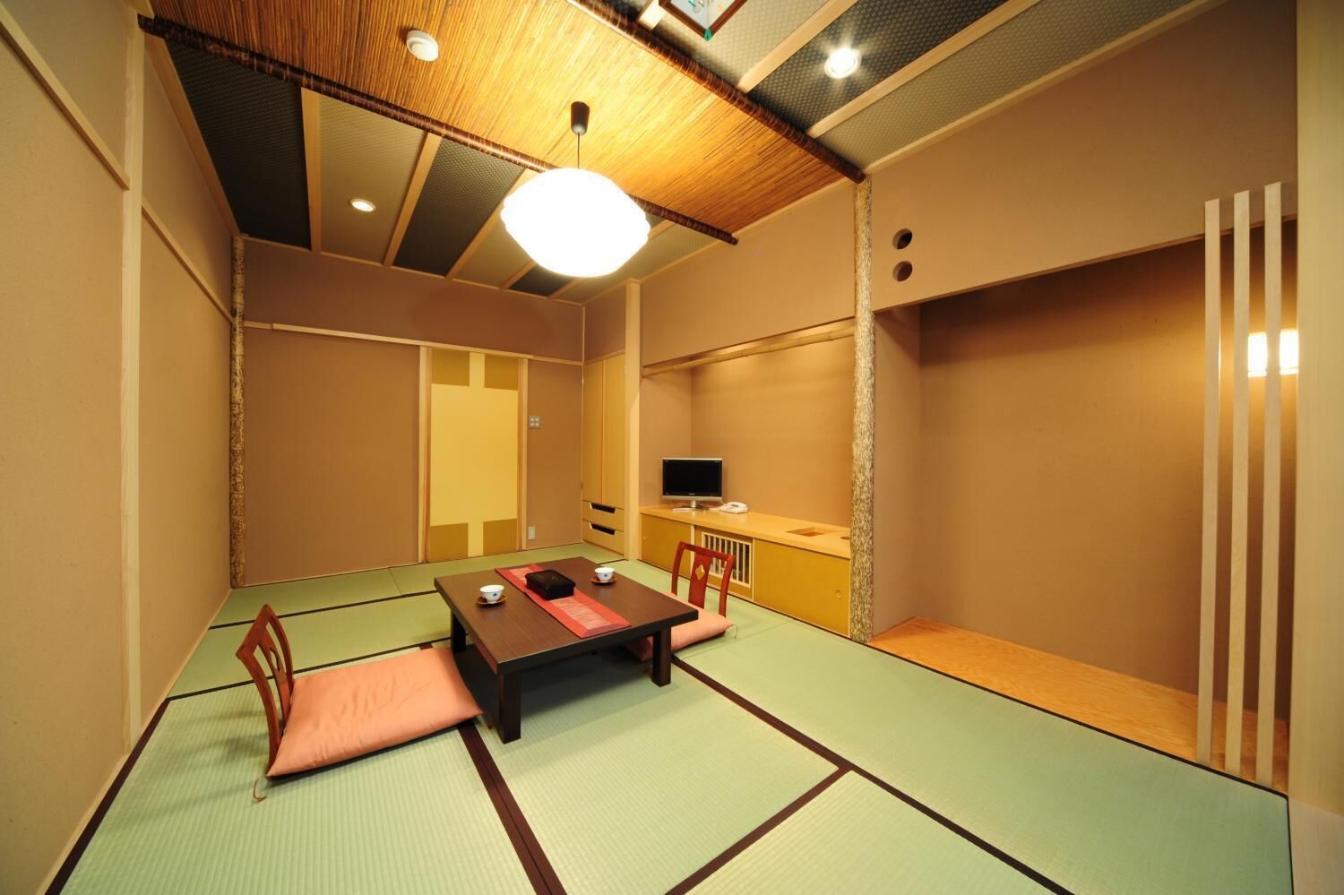 A traditional tatami mat room with a low table, cushions, a television, and sliding doors.