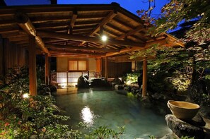 Ein traditionelles japanisches Onsen mit Holzbauweise und einem Steinbecken, umgeben von viel Grün.