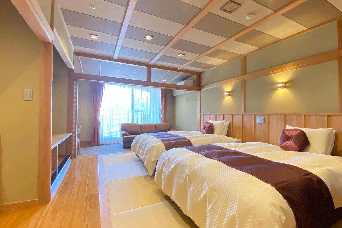 Ein Hotelzimmer mit einem großen Bett, einer Couch, einem Holzboden und Blick ins Freie.